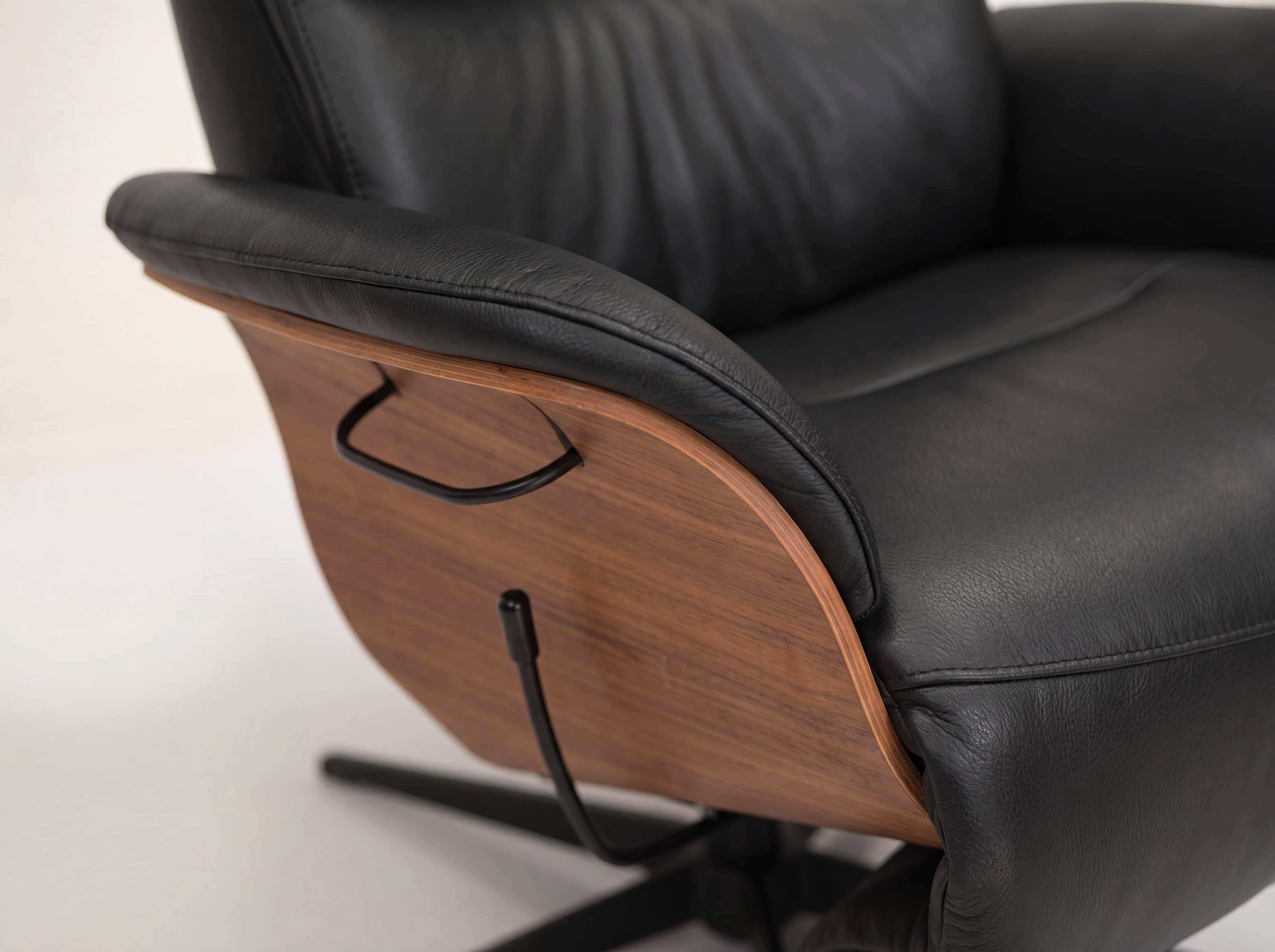 Relaxsessel mit schwarzem Lederbezug, geschwungener Holzschale und sichtbarem Metallgriff