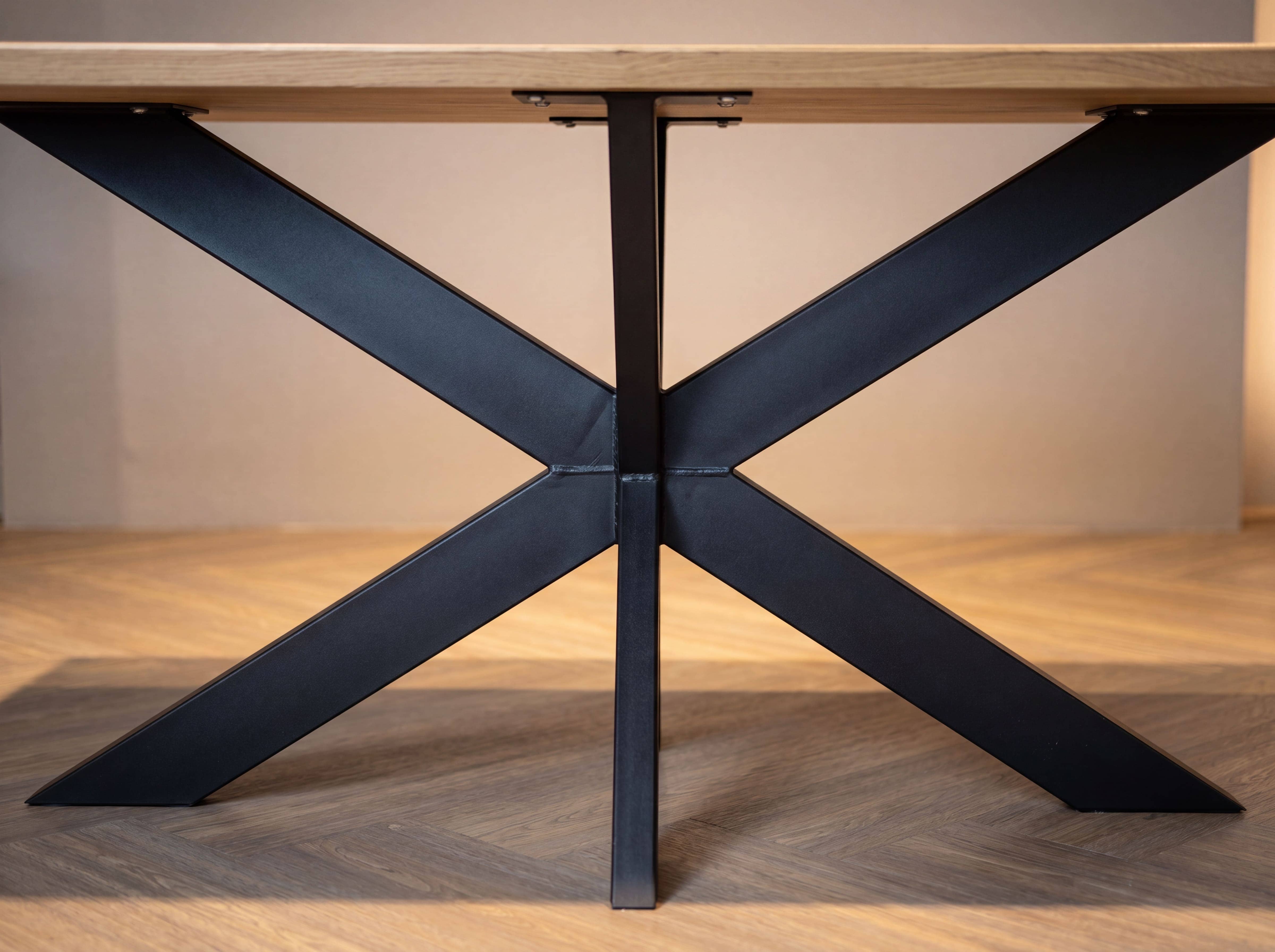 Esstisch mit rechteckiger Holzplatte und schwarzem Metallgestell in Kreuzform frontal fotografiert.