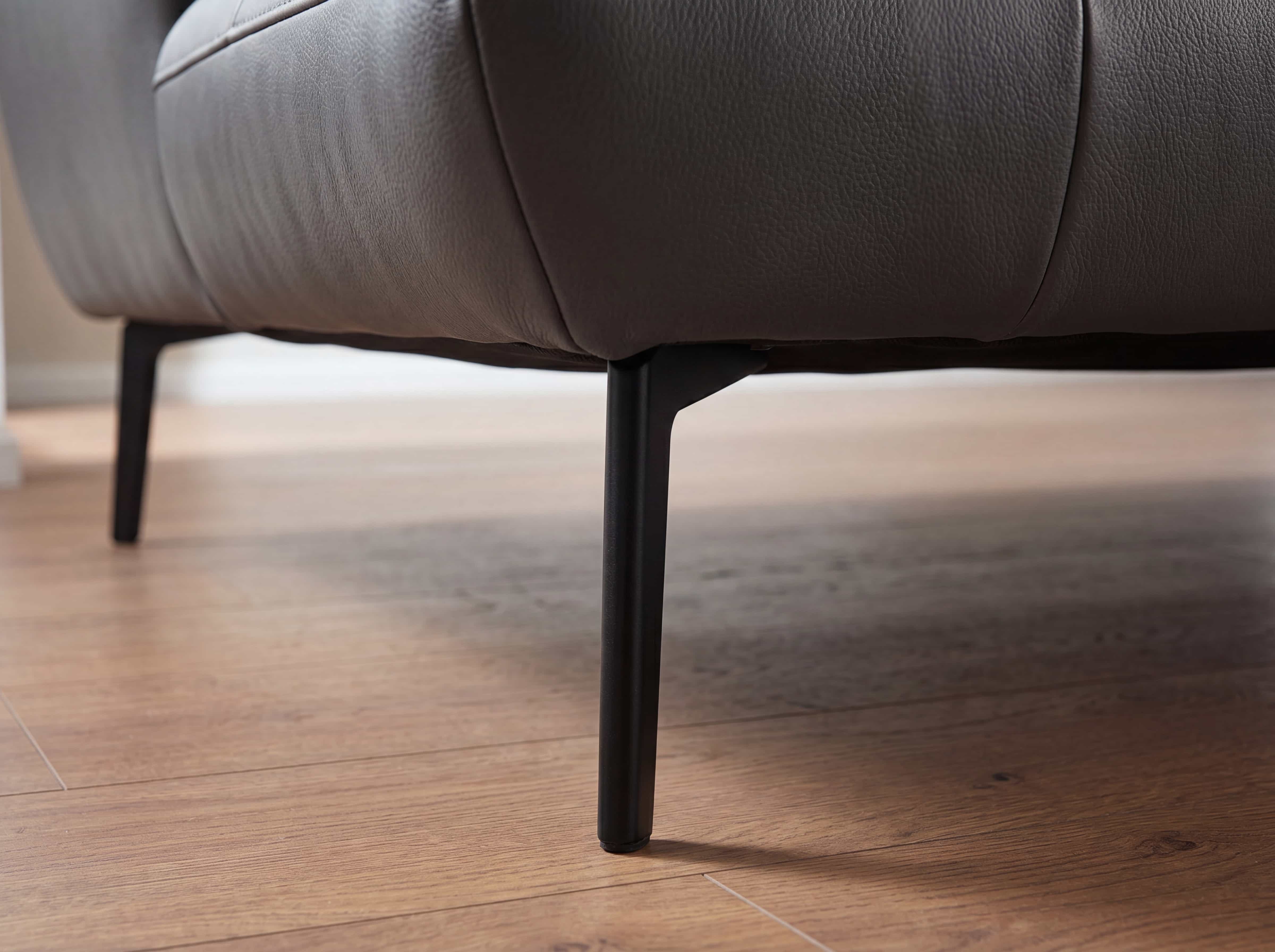 Sofa mit braunem Lederbezug und schwarzen, schlanken Metallfüßen auf Holzfußboden aus der Seitenansicht