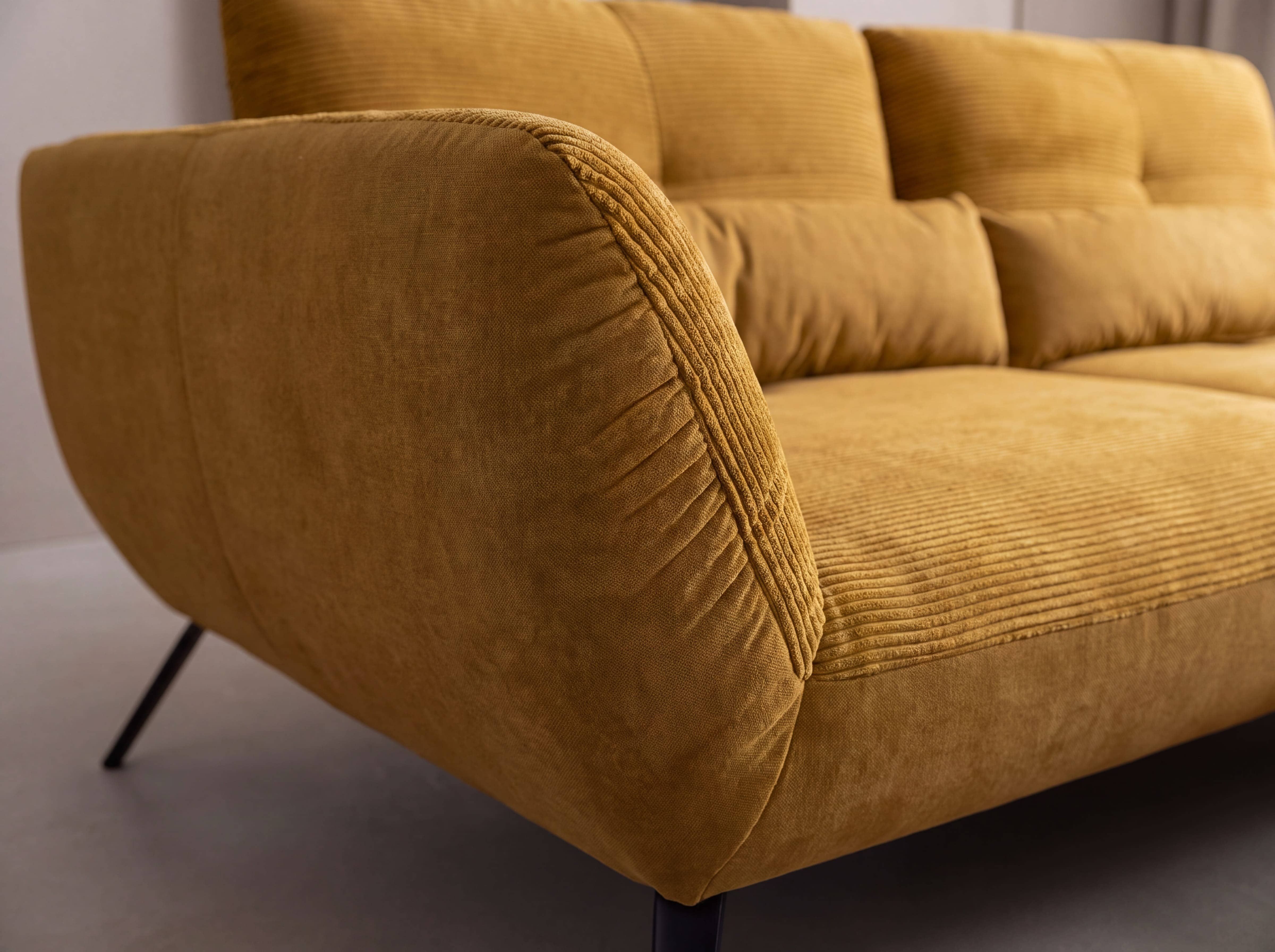 Ecksofa Paola – Detailansicht mit gelbem Cordbezug, markanter Armlehne und schwarzen Füßen