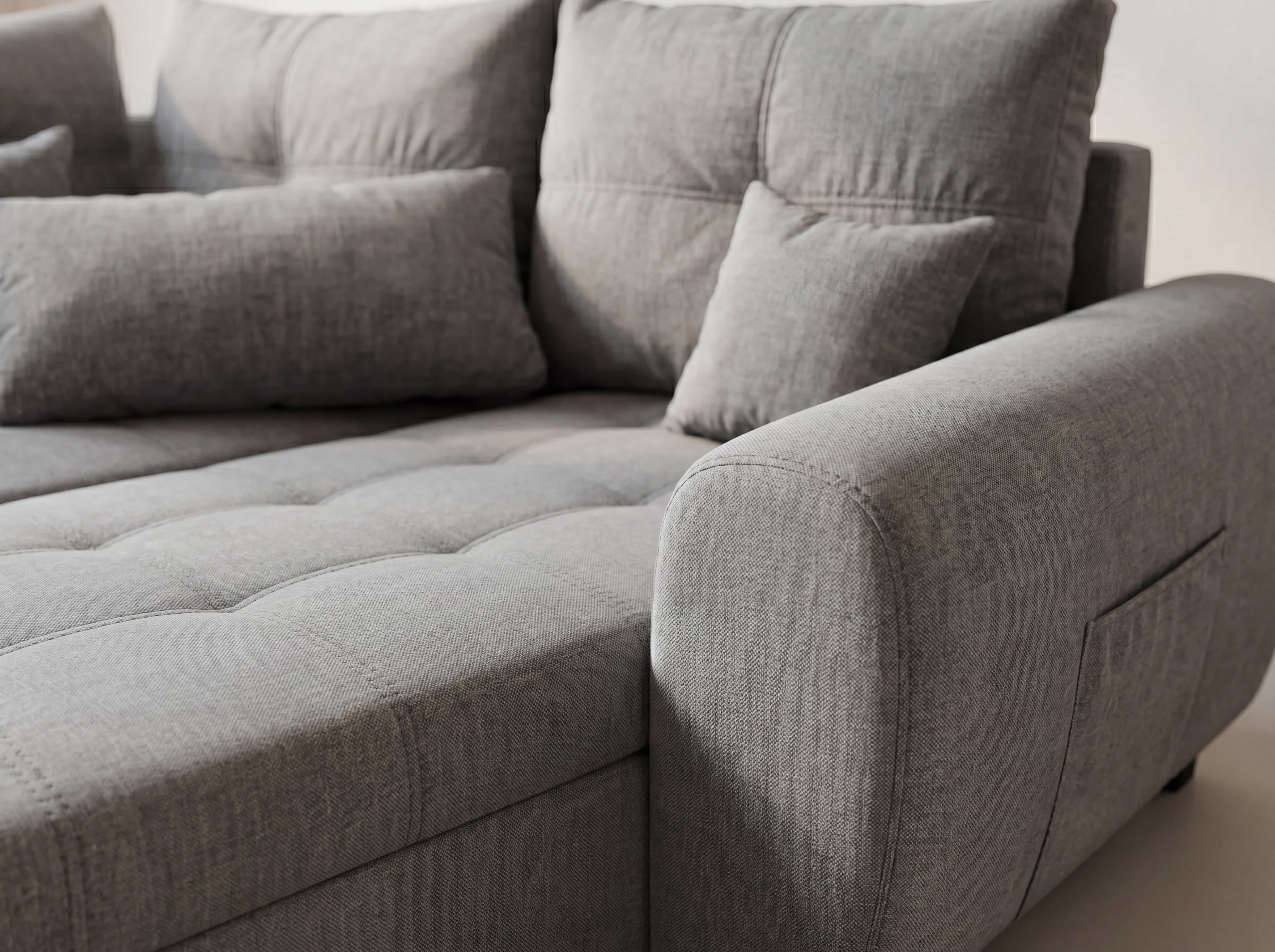 Ecksofa Dakota mit grauem Stoffbezug, breiter Armlehne, sichtbarer Steppung und Kissen