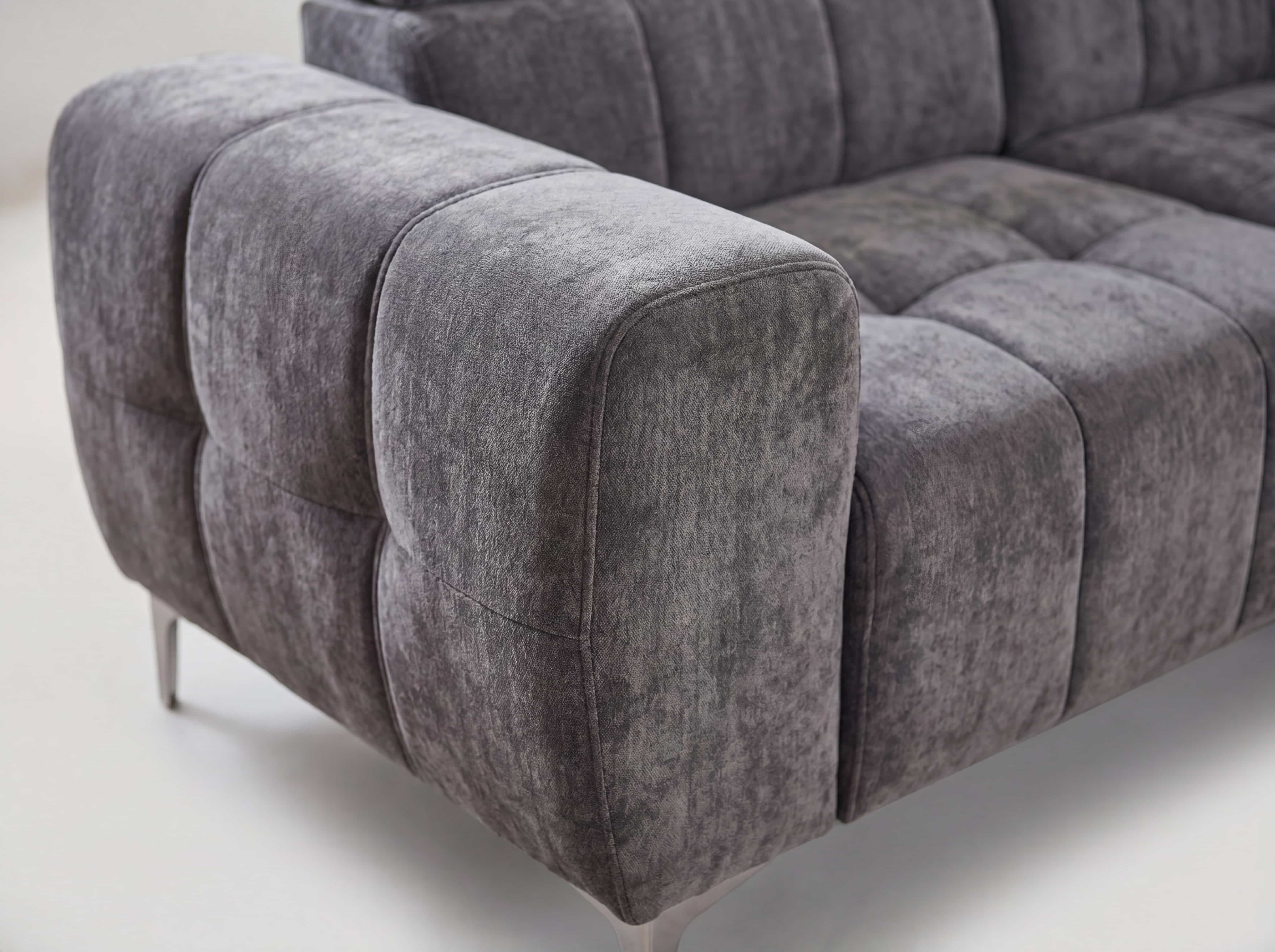 Ecksofa Kabs mit grauem Stoffbezug, markanter Polsterung und schmalen Metallfüßen, Armlehne sichtbar