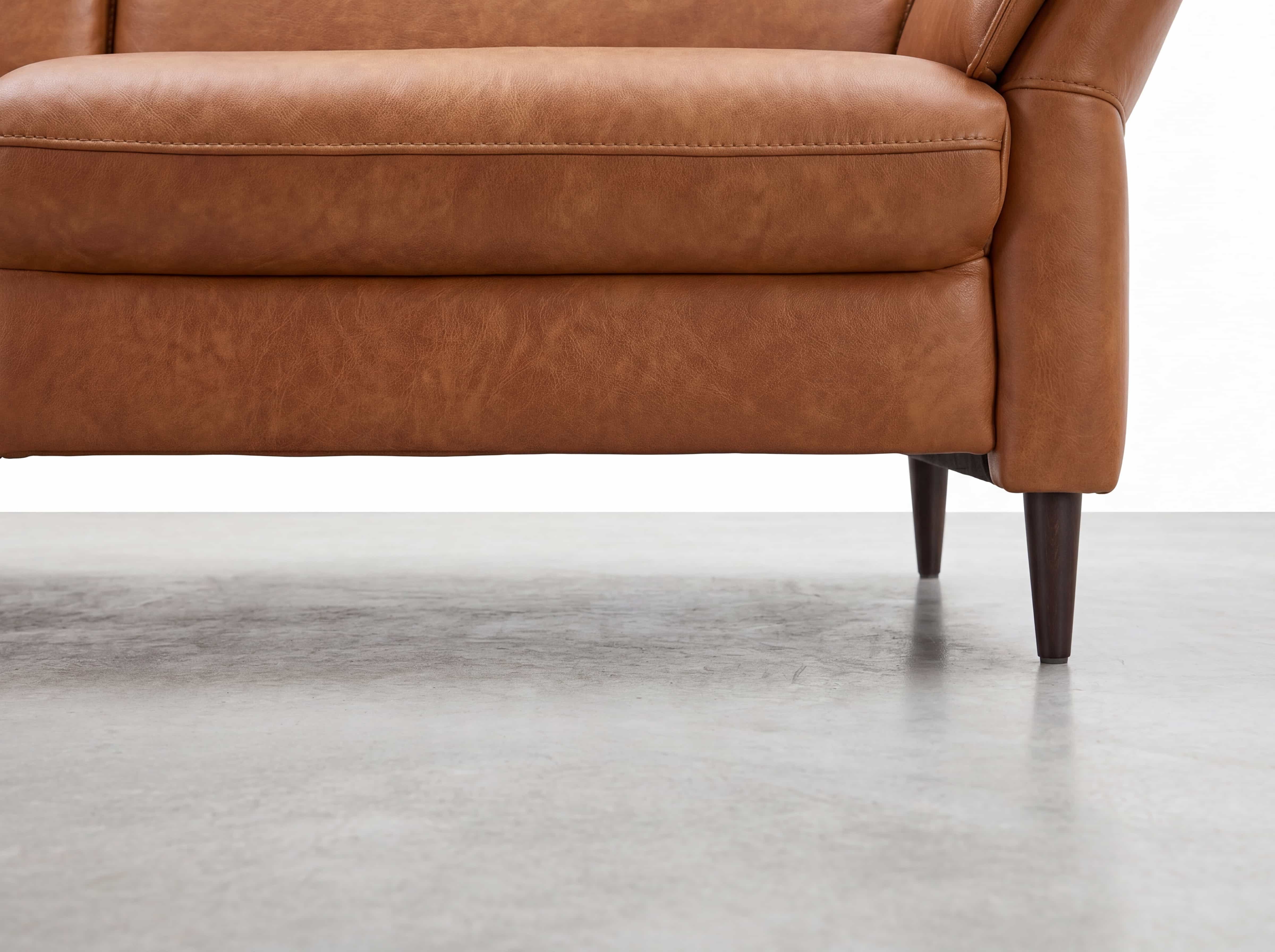 Ledersofa in Cognac mit konischen Holzfüßen und abgerundeter Armlehne, Detailansicht vorne