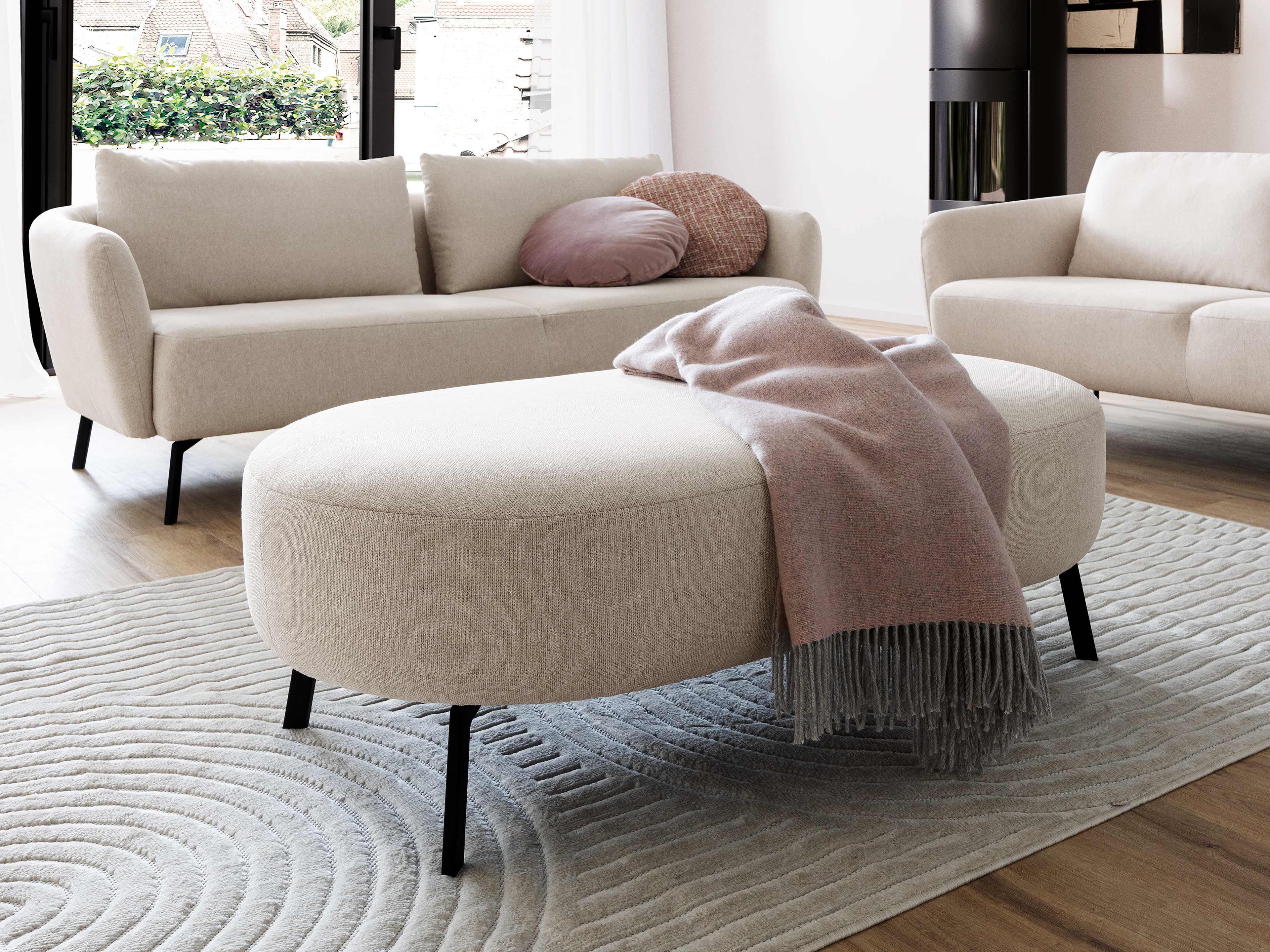 Ovaler Polsterhocker Kabs in Beige mit Stoffbezug und schwarzen schrägen Beinen auf Teppich