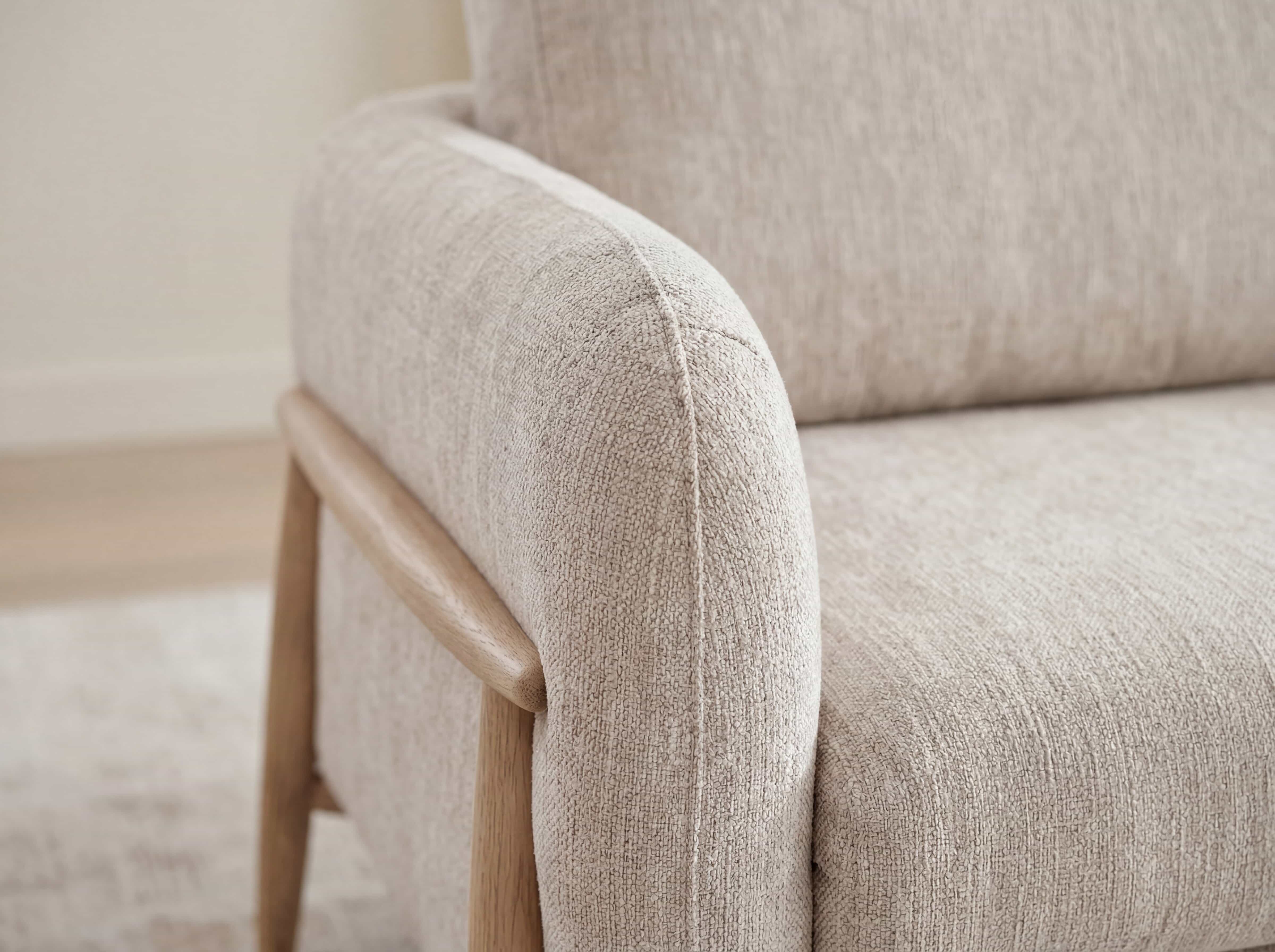 Armlehne eines Sofas mit beigefarbenem Stoffbezug und seitlichem Holzgestell in hellbraun.