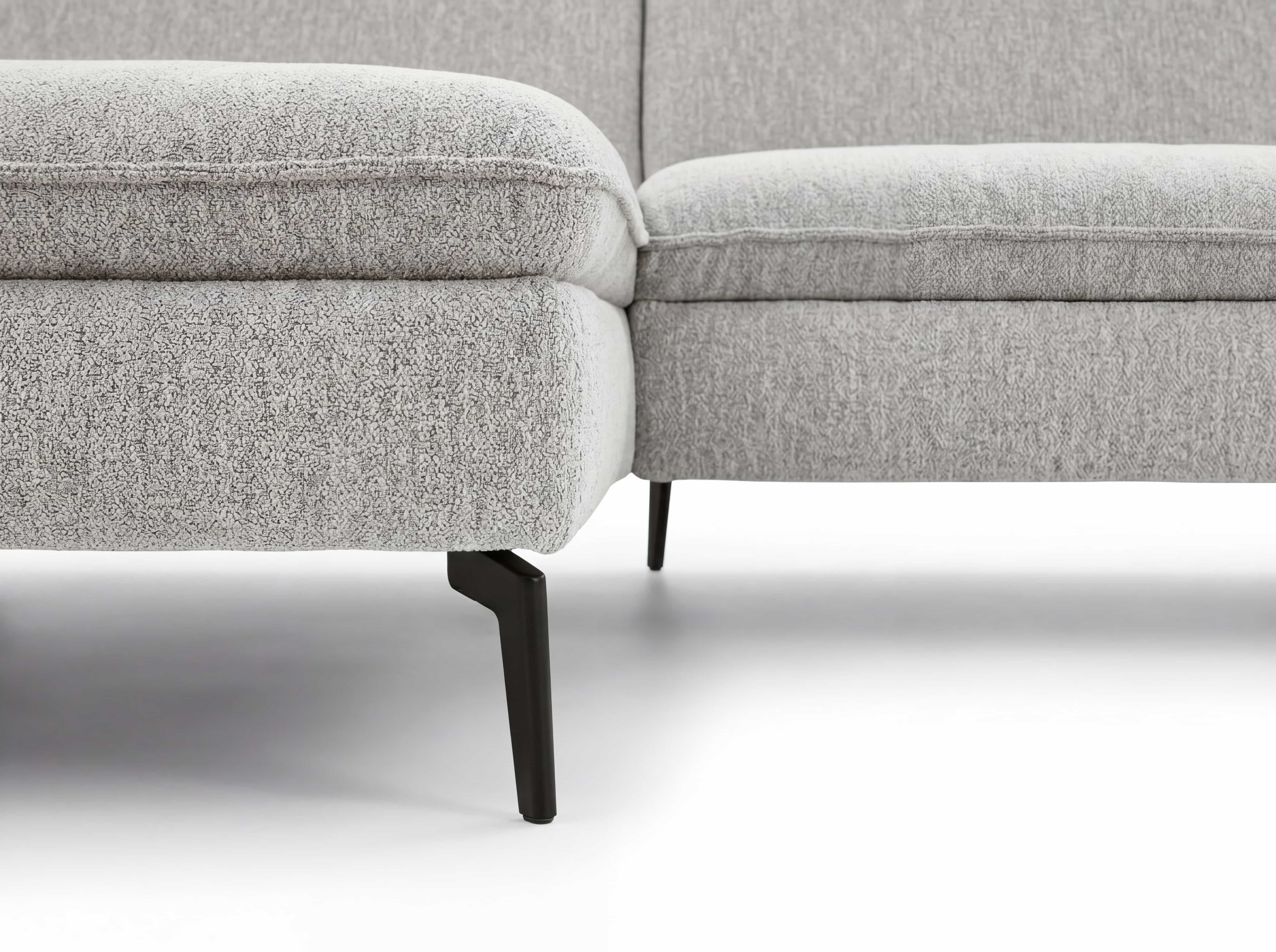 Ecksofa mit hellem Stoffbezug, gepolsterten Sitzflächen und schwarzen Metallfüßen in Nahaufnahme