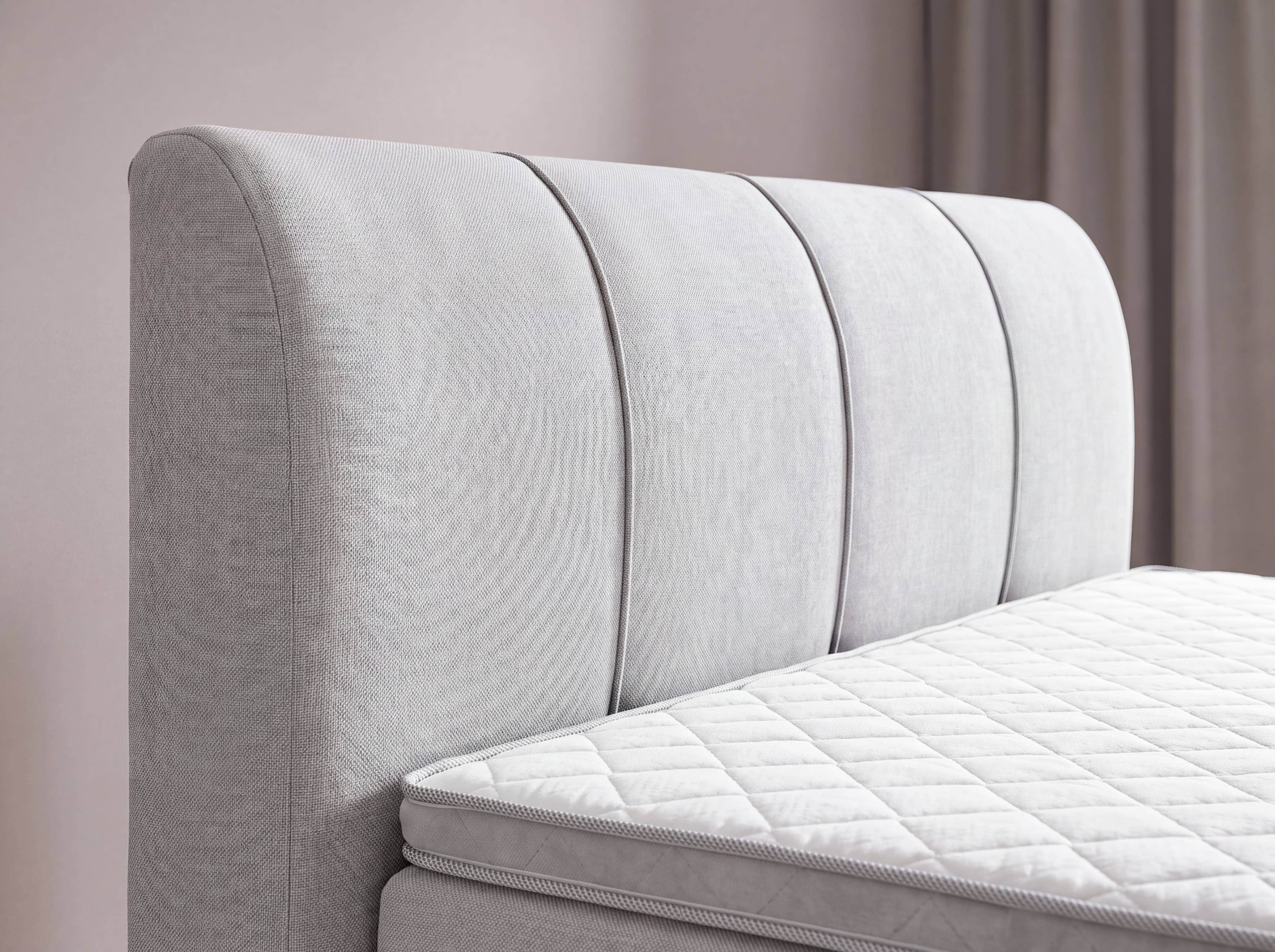 Boxspringbett mit hellgrauem, strukturiertem Stoffbezug, gestepptem Kopfteil und sichtbarer Matratze