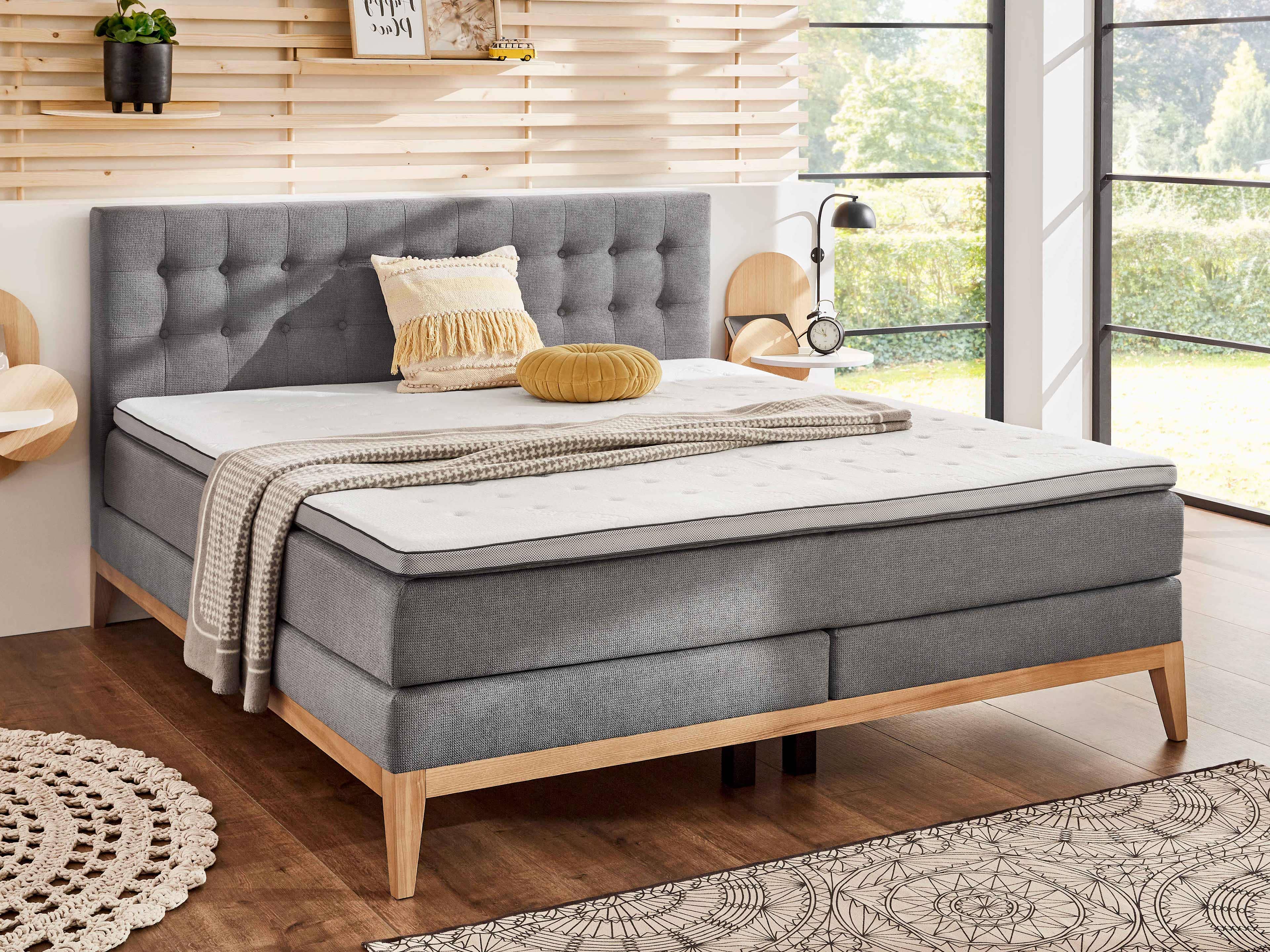 Boxspringbett Kabs mit grauem Stoffbezug, gepolstertem Kopfteil und Massivholzfüßen, Frontansicht