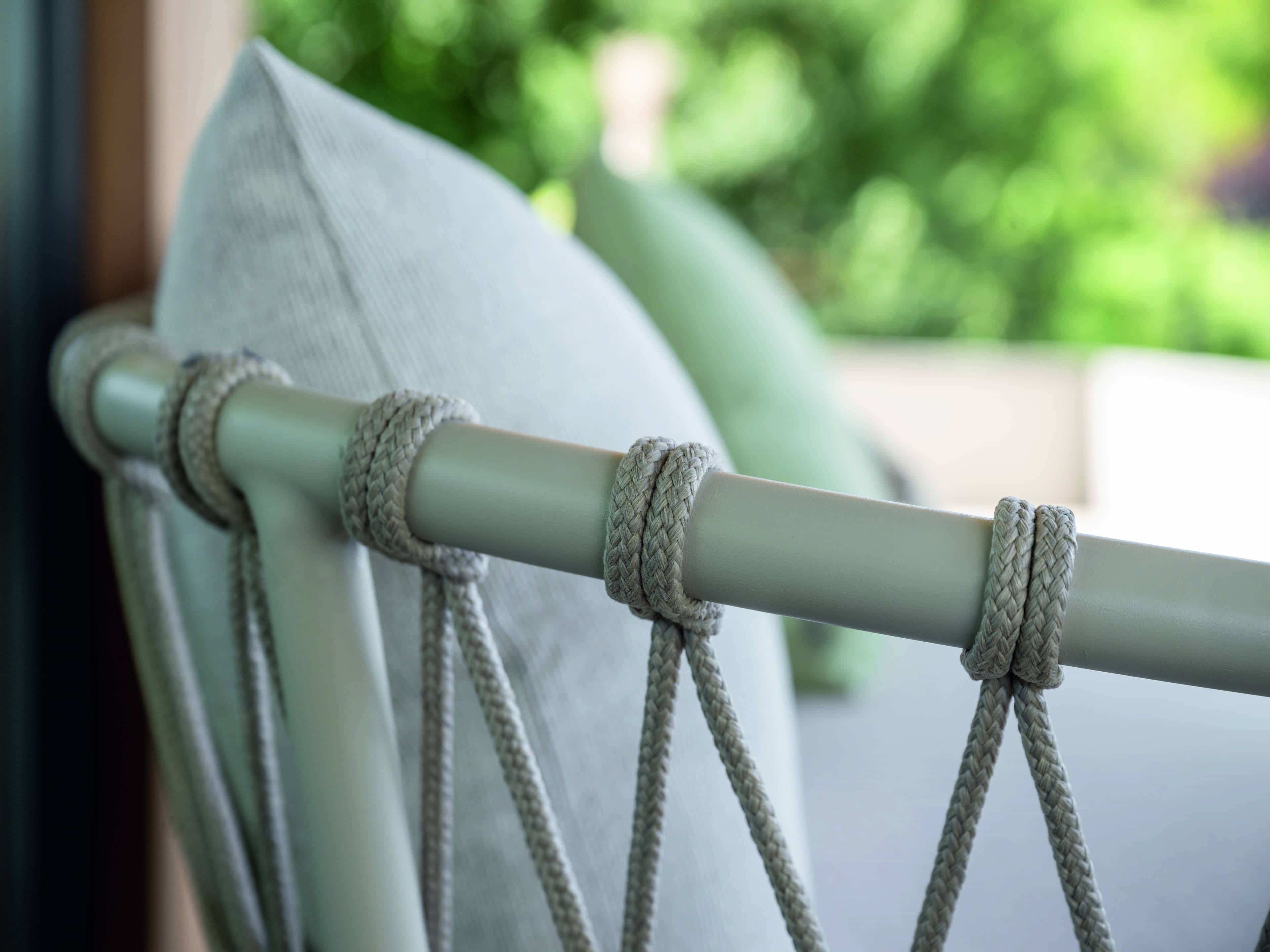 Detailaufnahme einer Rückenlehne mit heller Polsterung, Metallgestell und geflochtenen Textilseilen