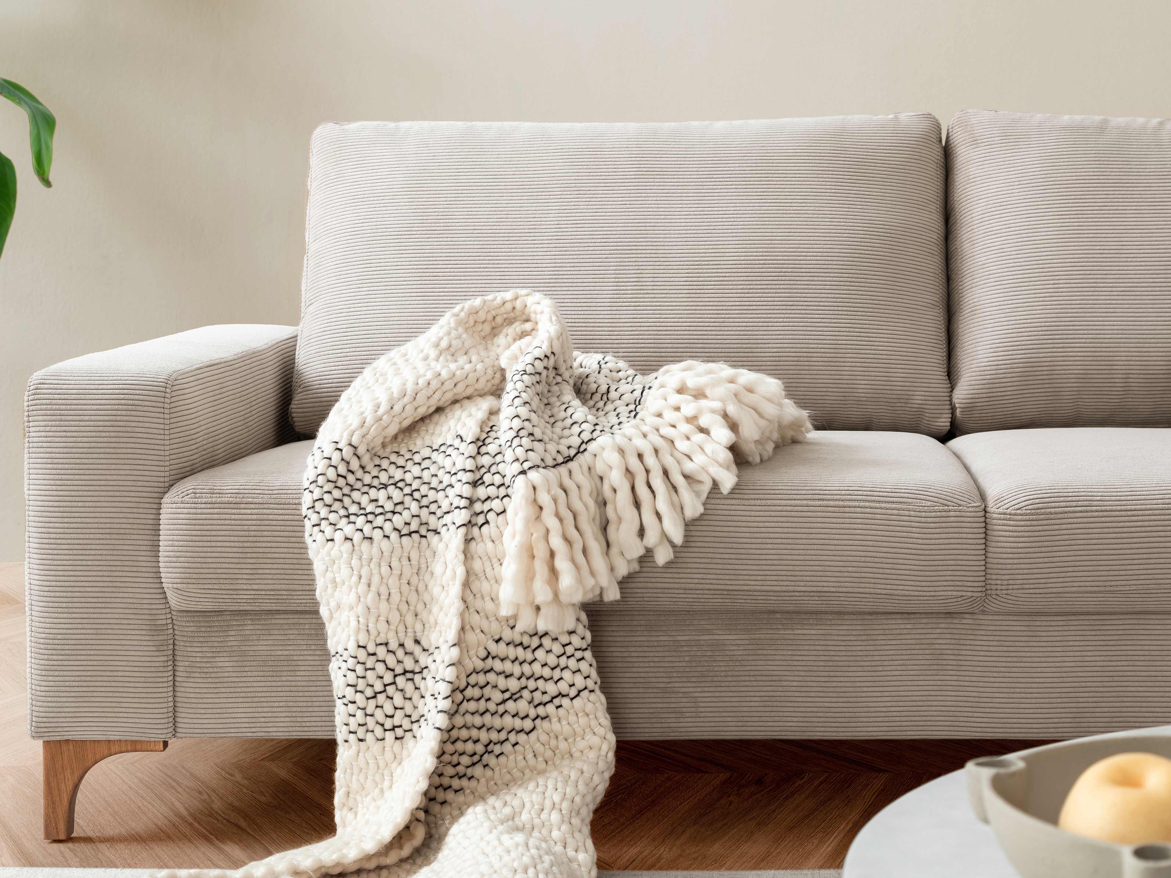 2-Sitzer Sofa mit hellbeigem, geripptem Stoffbezug, Holzfüßen und rechter Armlehne, frontal fotografiert
