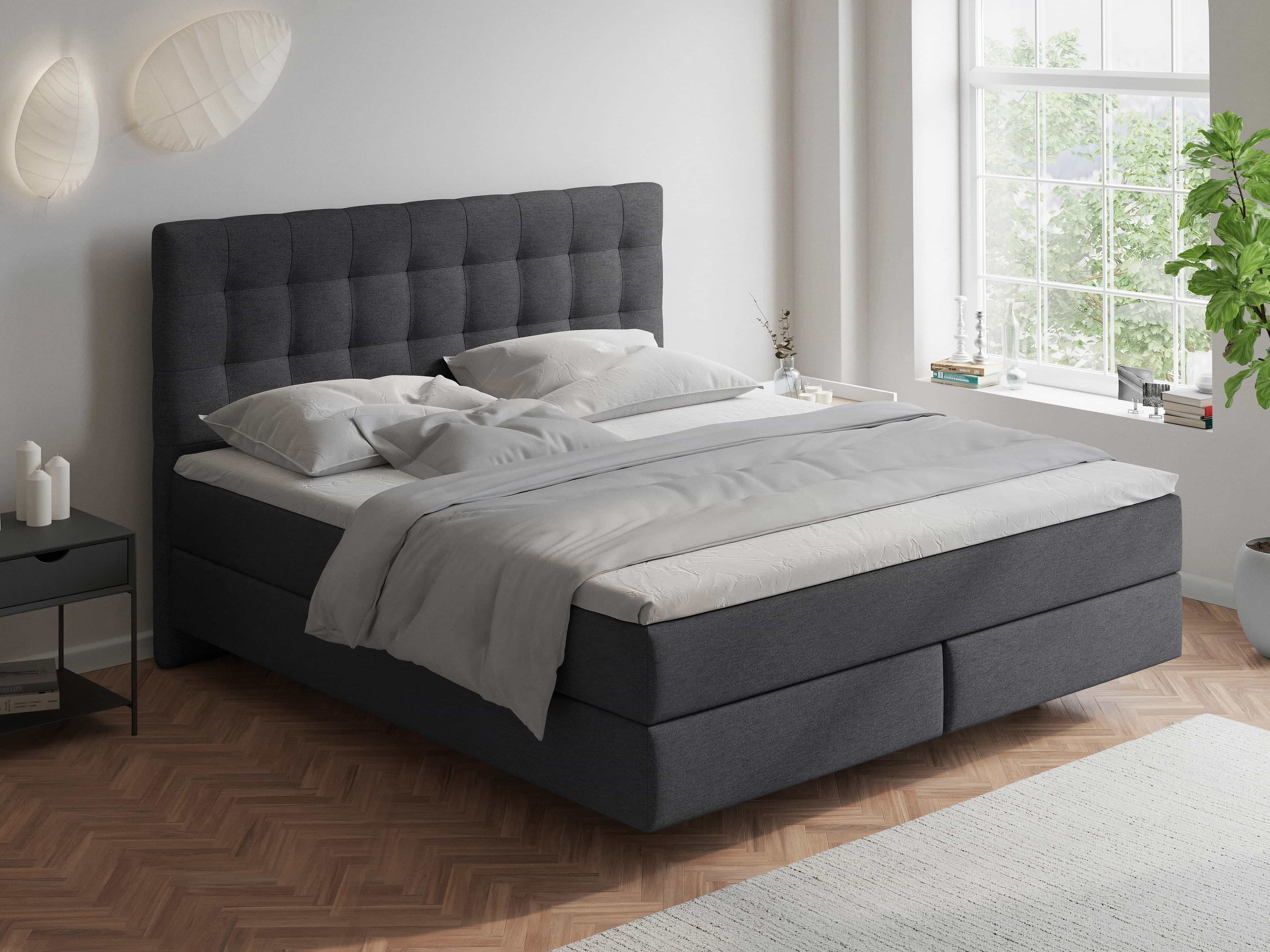 Boxspringbett Kabs Polsterwelt in dunkelgrauem Stoff mit gepolstertem, gestepptem Kopfteil.