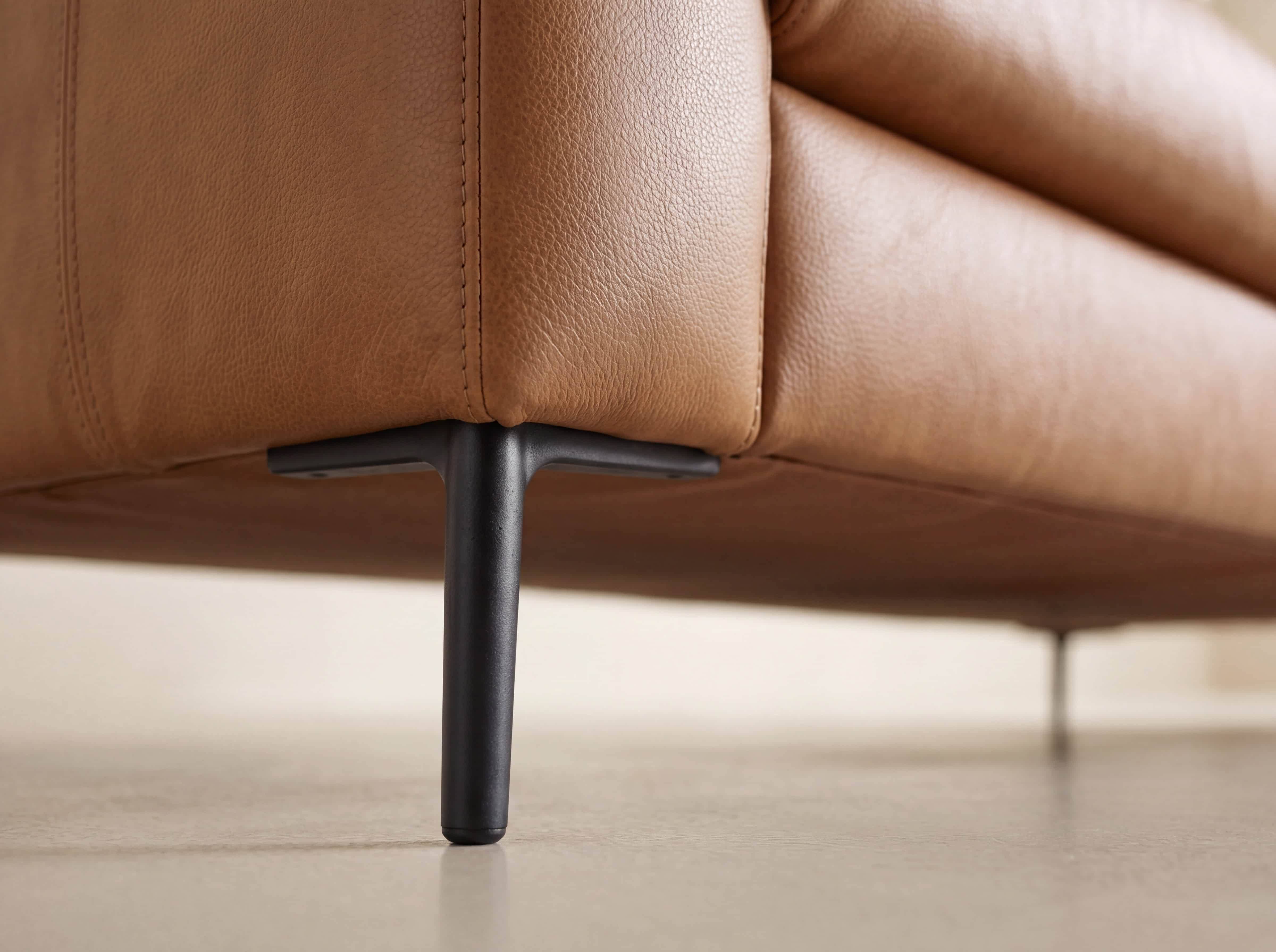 Detailansicht eines Sofafußes aus schwarzem Metall und cognacfarbenem Lederbezug