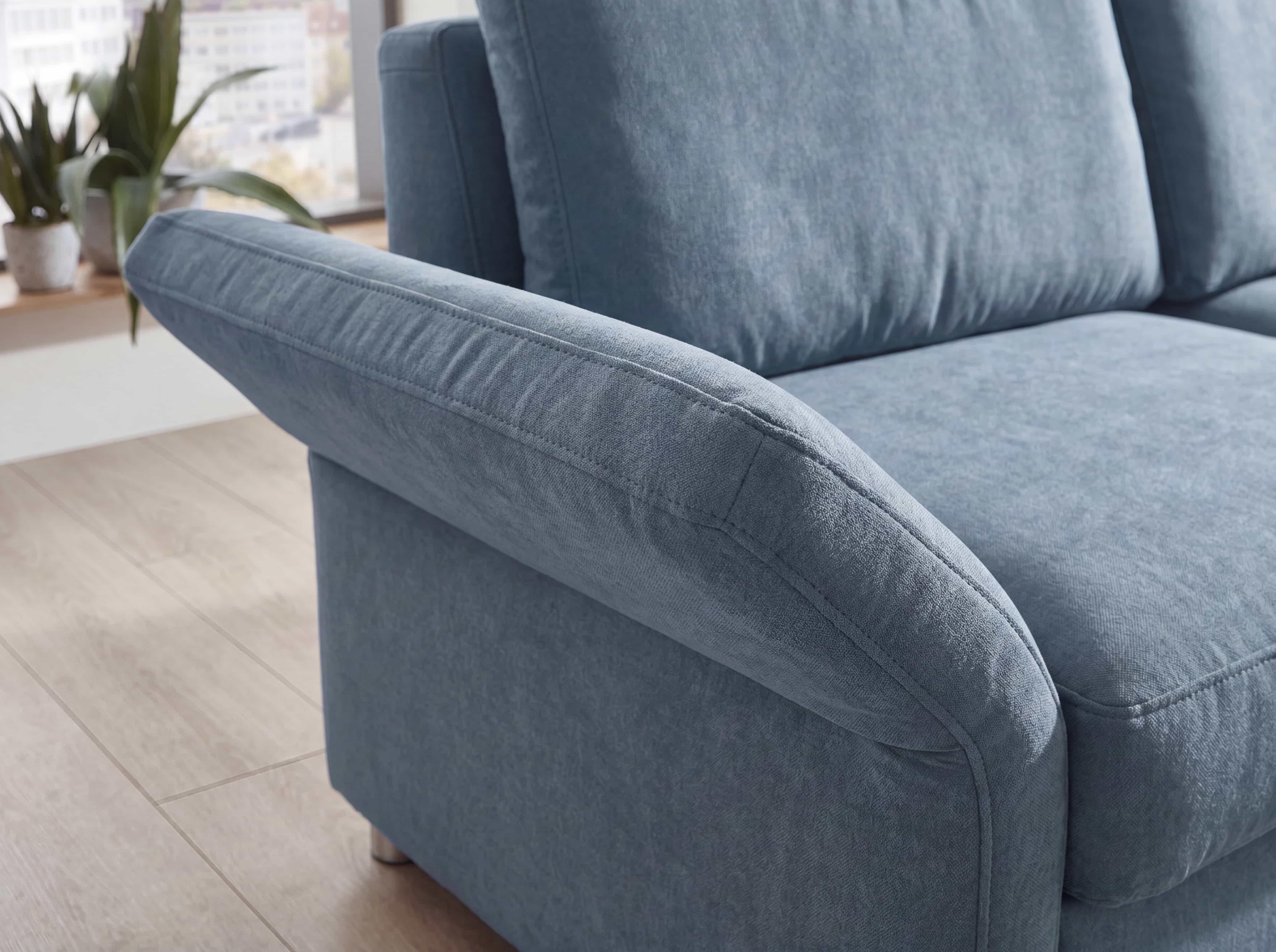 Ecksofa mit breiter, gepolsterter Armlehne aus blauem Stoffbezug und sichtbarer Steppnaht