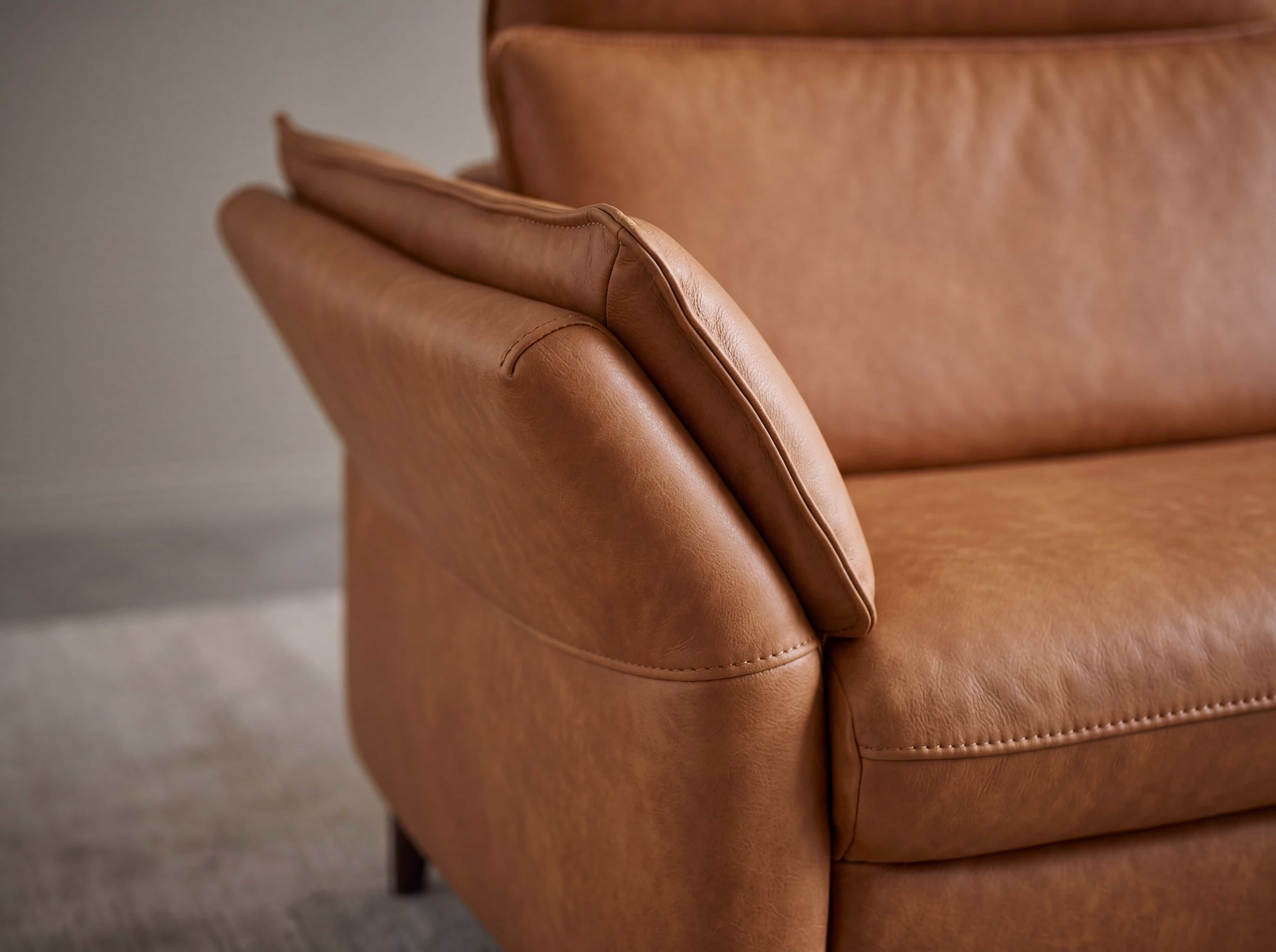 Detailaufnahme eines braunen Ledersofas mit seitlicher, gepolsterter Armlehne und sichtbarer Naht