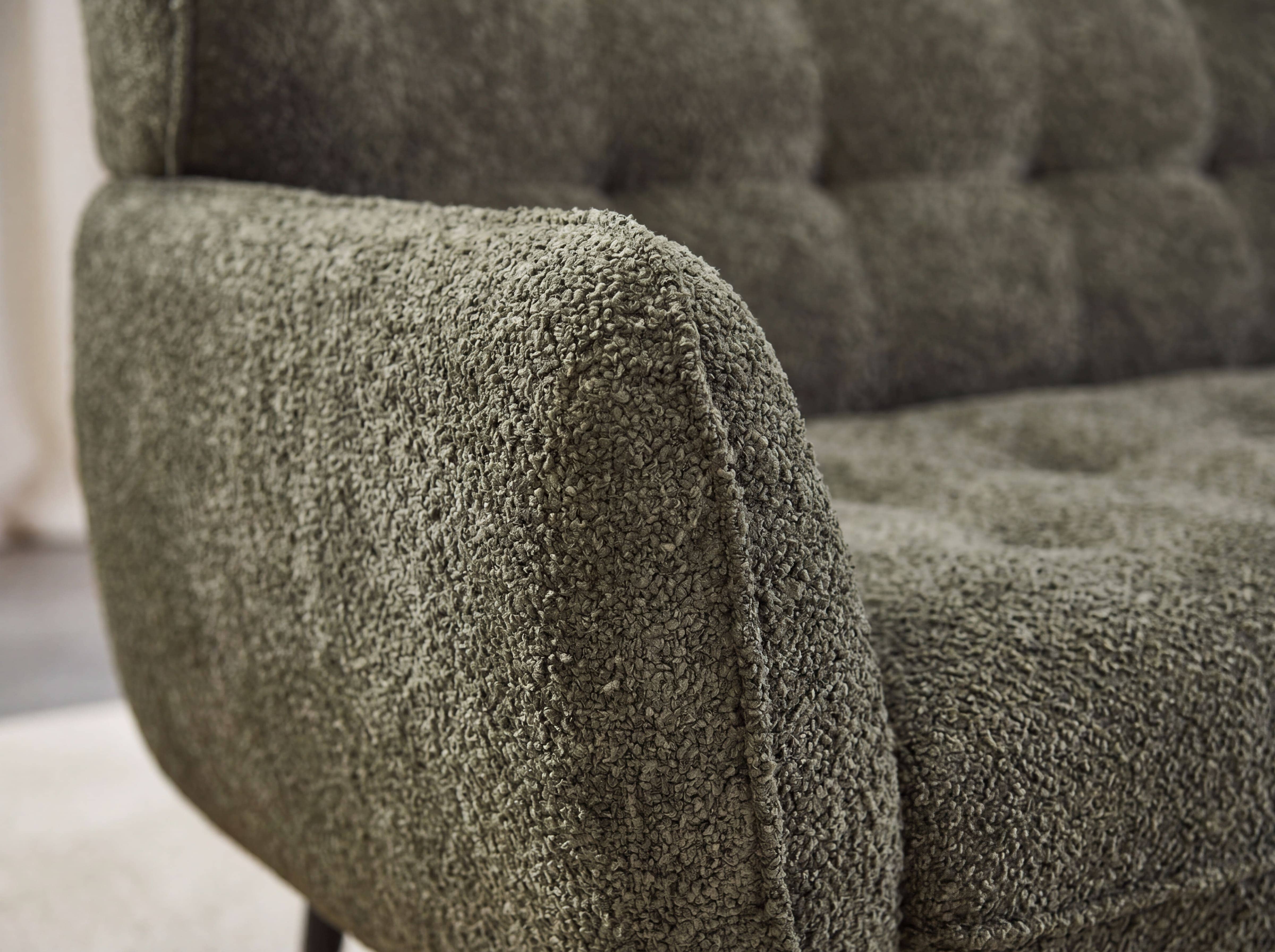 Detailaufnahme eines Sofas mit Armlehne in grünem Bouclé-Stoff und sichtbarer Polsterstruktur.